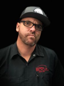 A man wearing glasses and a hat is standing in front of a black background.