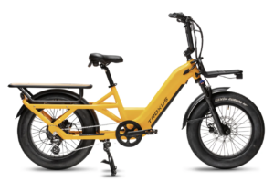 Yellow electric cargo bike with a black saddle, front and rear racks, wide tires, and a kickstand. The bike has "Troxus" branding on the frame, blending utility with performance akin to high-end road bikes like Colnago or Orbea.